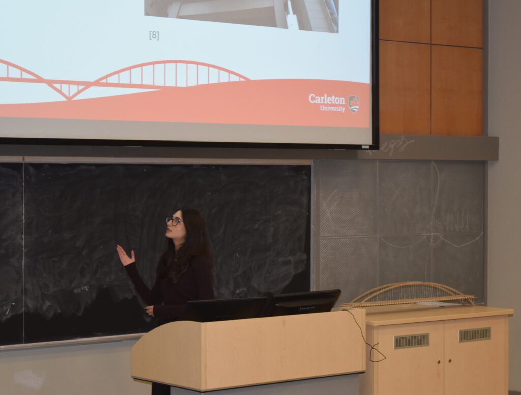 Photo shows Hala Al Shawa presenting their group's capstone project in front of a lecture hall in formal clothing. 