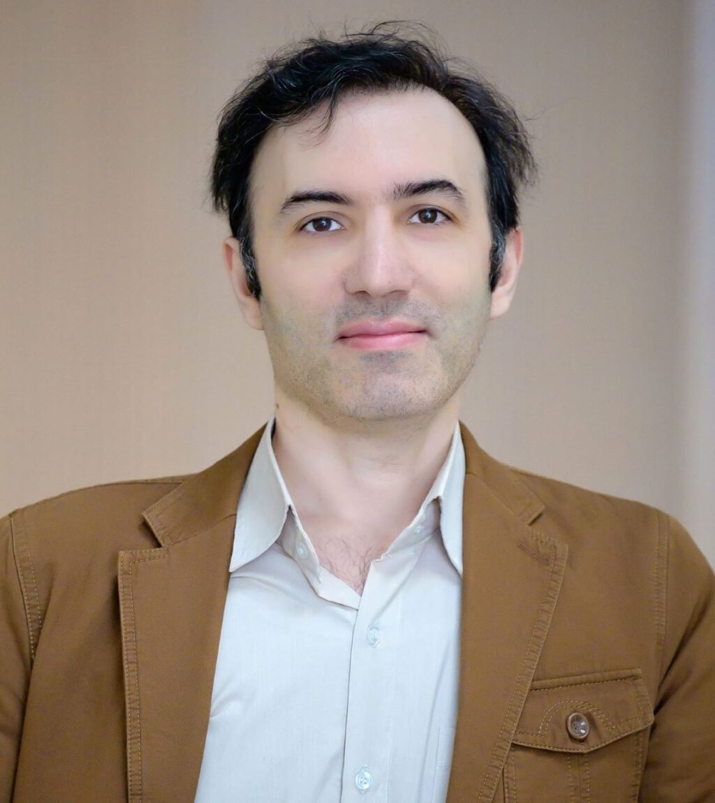 Professor Hamzeh Hajiloo posing for a headshot in a brown jacket with a white shirt underneath