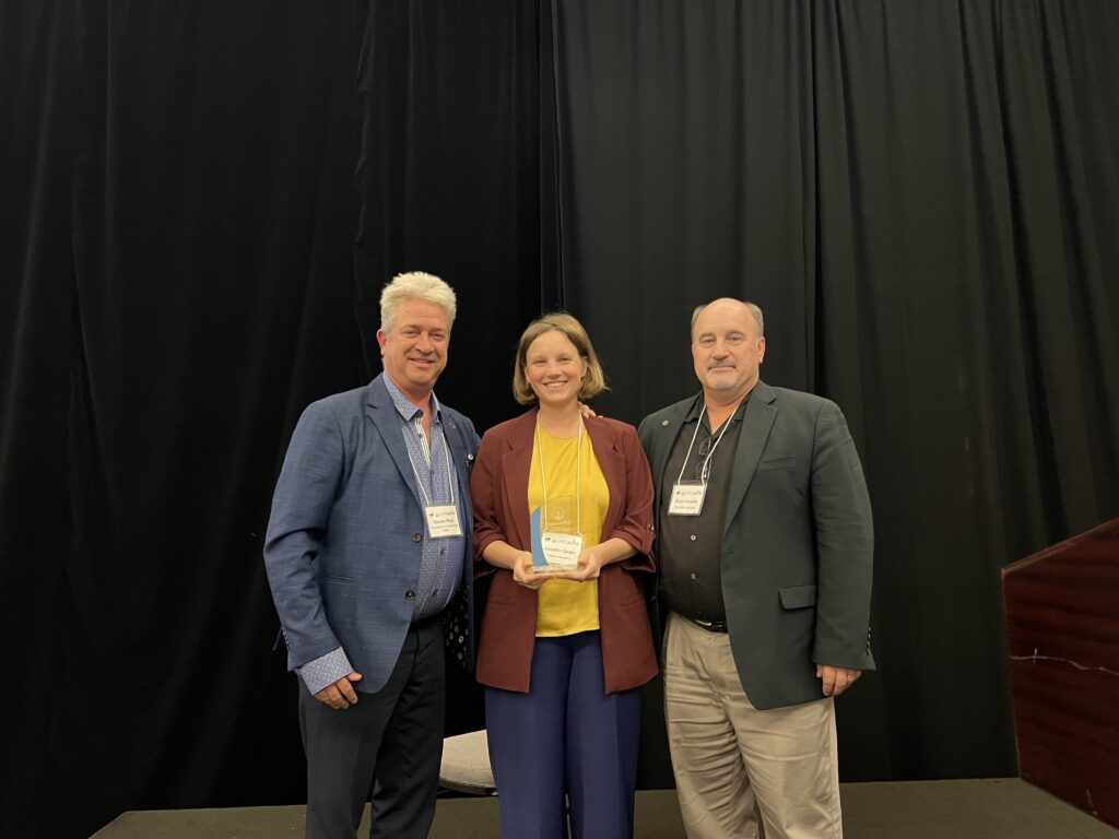 Image shows Dr. Jennifer Drake holding her award standing next to two men in suits.