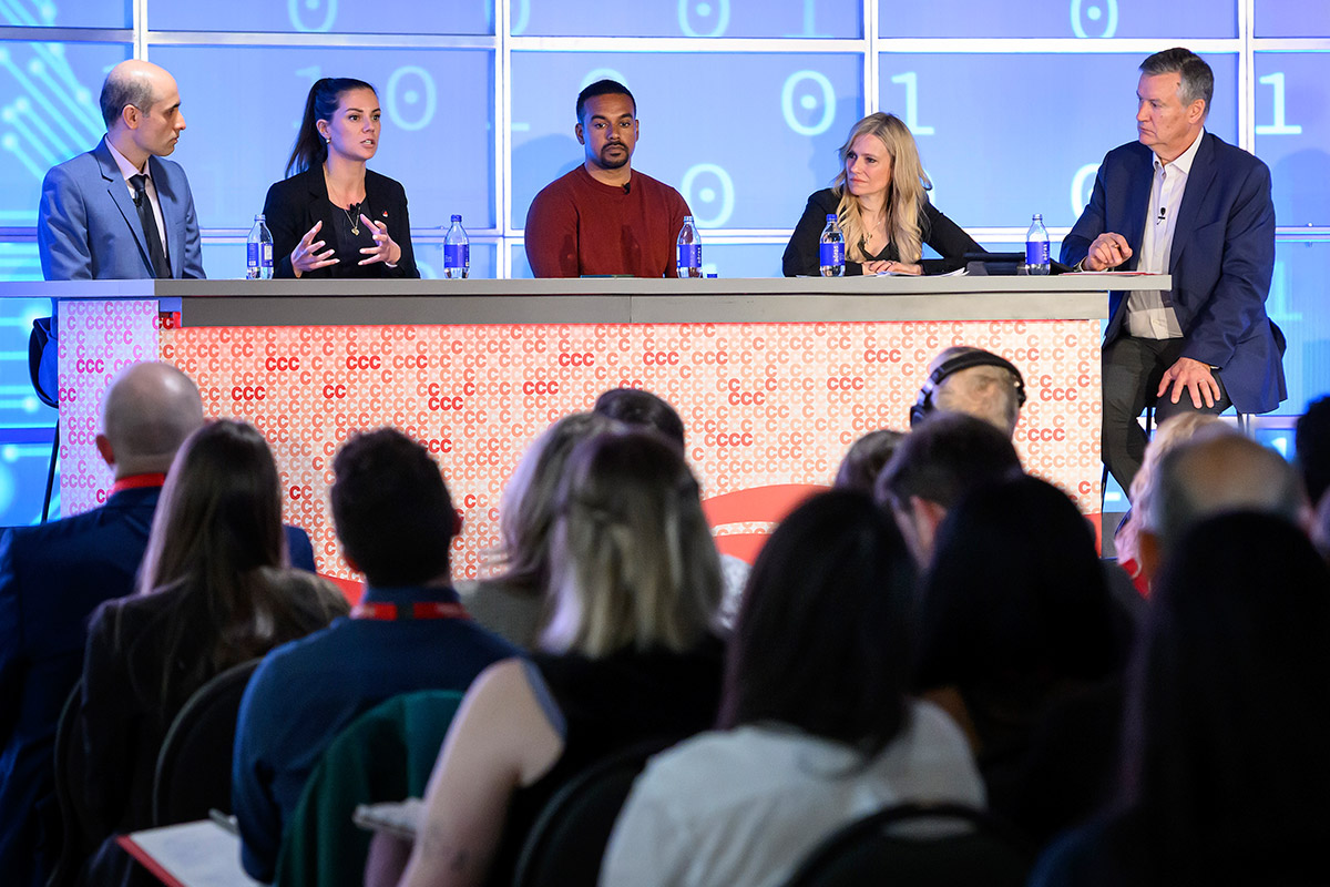 Five people sitting at a table, taking part in a panel discussion with an audience in the foreground.