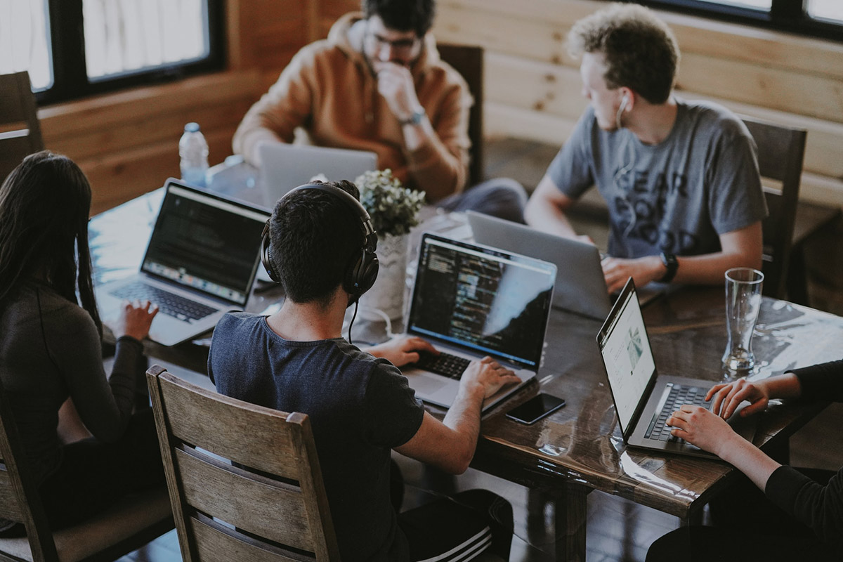 Four people sitting at a rectangular table, working on laptops.