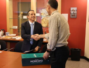 Two men shaking hands. A decorative blue/green box rests on a table in front of them.
