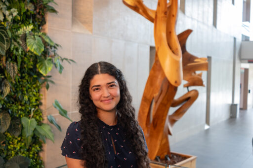 Ayssa Mandarino sits in front of a plant wall and sculpture in a building at Carleton University.