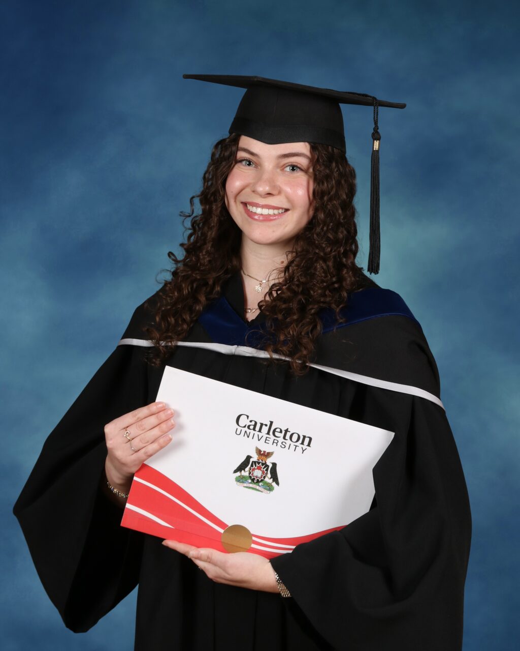 Gabby Makovka in a Convocation robe with her Carleton University degree in her arms.