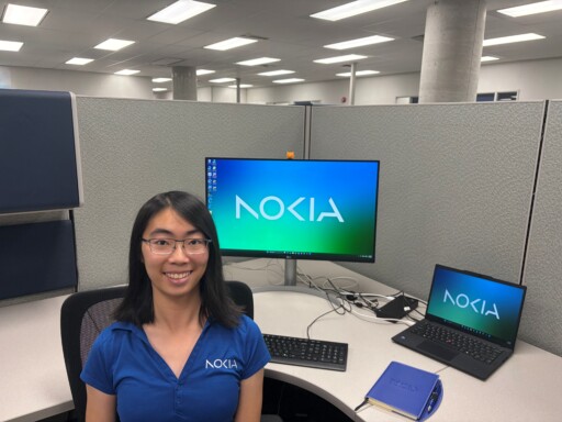 Fiona Cheng wears a blue Nokia shirt and sits at her desk in a cubicle. The screensaver on her desk says Nokia.