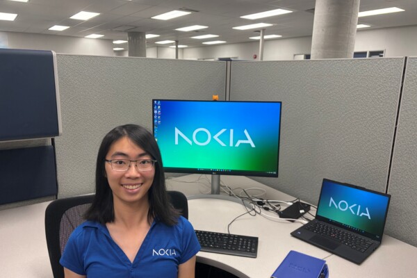 Fiona Cheng wears a blue Nokia shirt and sits at her desk in a cubicle. The screensaver on her desk says Nokia.
