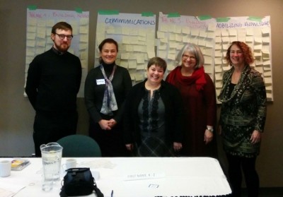 University of Victoria researchers from the KMb hub project pose in front of chart paper covered in brainstorming sticky-notes.