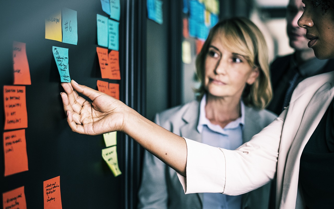 Two women rearrange sticky notes on the project management timeline.