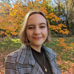 This is a headshot of Dunja Palin. She is wearing a black and grey plaid blazer with a black shirt. 