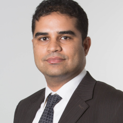 This is a headshot of Amar Benaissa. He is wearing a dark grey pin-striped suit, with a white dress shirt and black tie.