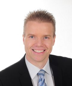 This is a headshot of Daniel Gulanowski. He is wearing a black suit, white dress shirt and blue-striped tie. 