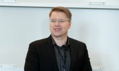 Dr. Daniel Gulanowski wearing black business attire, in front of a whiteboard