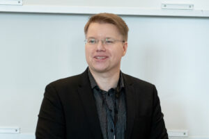 Dr. Daniel Gulanowski wearing black business attire, in front of a whiteboard