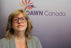 This is a portrait of a woman who has shoulder length blond hair, and who wears red glasses. Behind her, in the background, it says DAWN Canada.