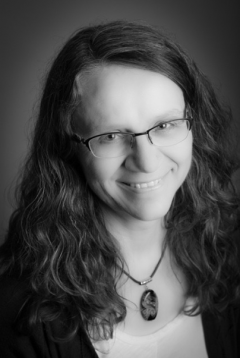 This is a black and white portrait. A woman has long wavy hair and wears glasses.