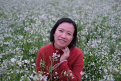 This is a picture of a woman with short black hair. There are a lot of flowers around her.