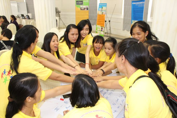 Girls and Women, who are wearing yellow shirts, joining hands in a circle.