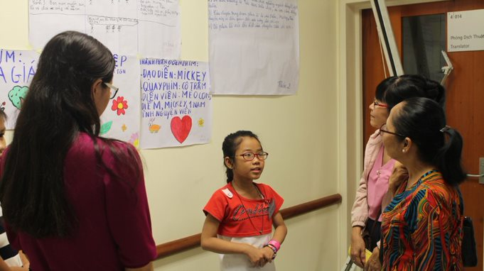 There is a girl introducing her group’s cellphilm to guests. Behind her is the brainstorming of the cellphilm.