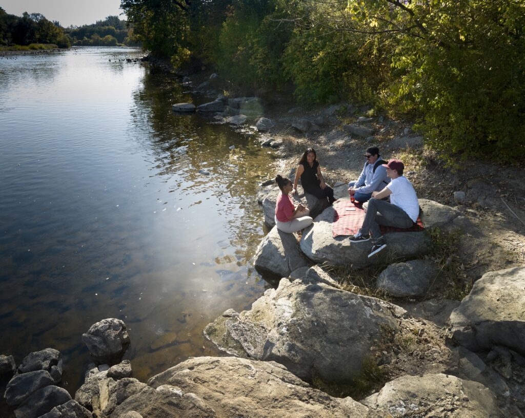 Several people sitting on rocks on a riverbank.
