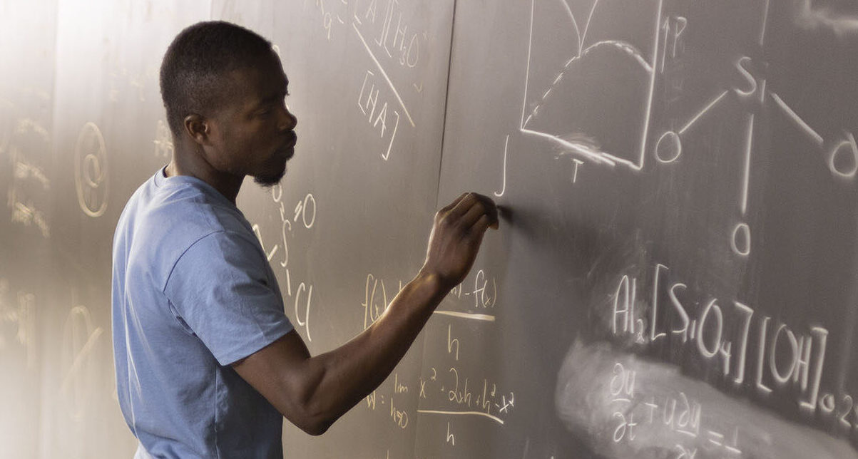 man at chalkboard writing formulas