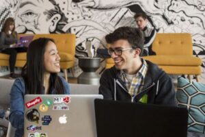 two students talking with computer in a study space