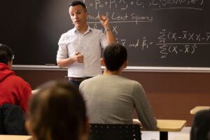professor teaching math formulas in front of classroom of students