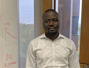 ph.d. student standing beside whiteboard with formula and windows
