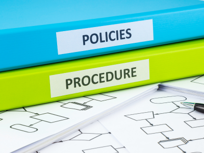 Blue policy binder on top of a lime green procedure binder laying on a pile of papers