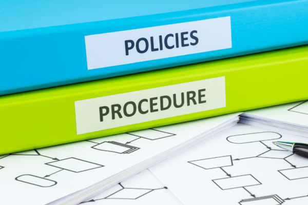 Blue policy binder on top of a lime green procedure binder laying on a pile of papers