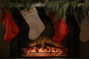 Red and white stockings hung on a fireplace with a fire burning underneath.