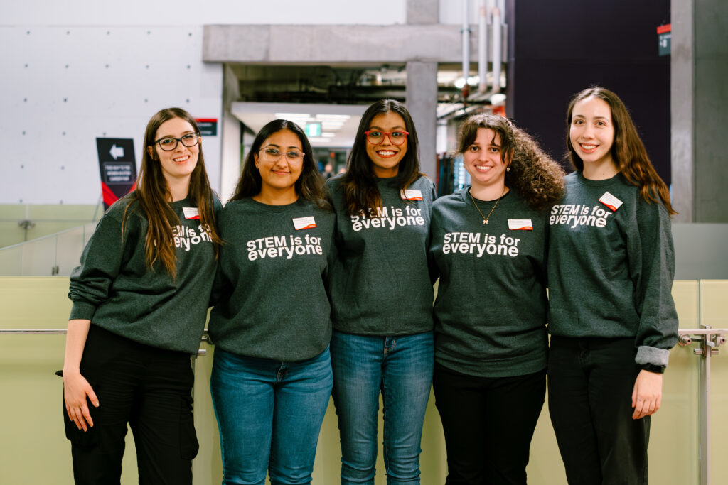 Group of five Graduate Assistants at the WiE&IT Program wearing a grey t-shirt that reads "STEM is for everyone."