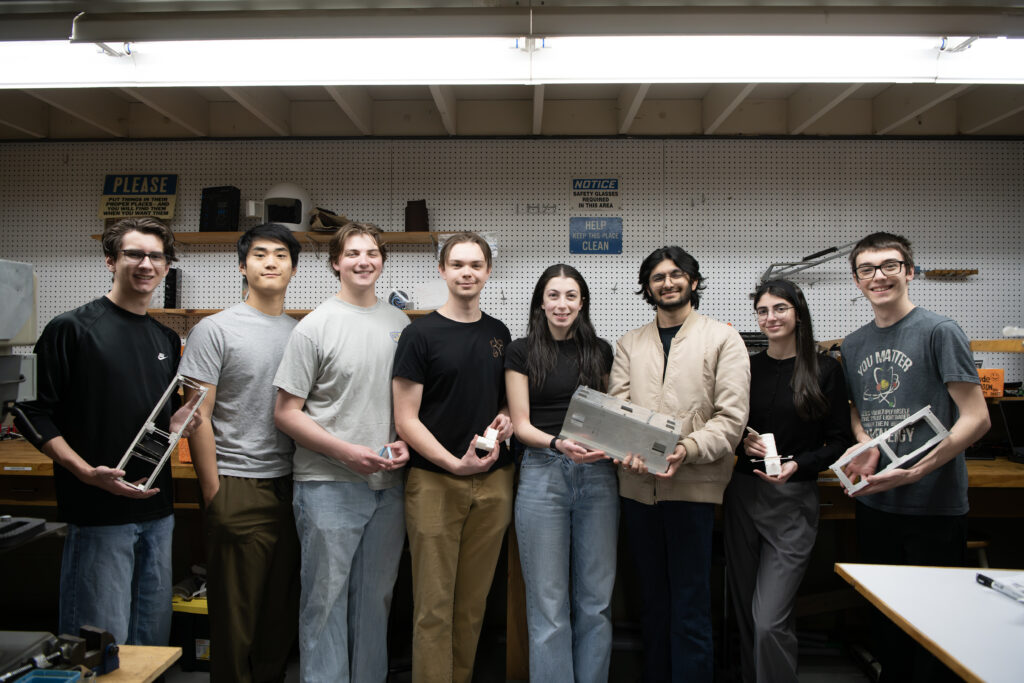 Members of CUonOrbit in their workspace holding components and 3D printed models of of a CubeSat