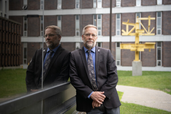 Ron Miller standing outside next to a window showing his reflection