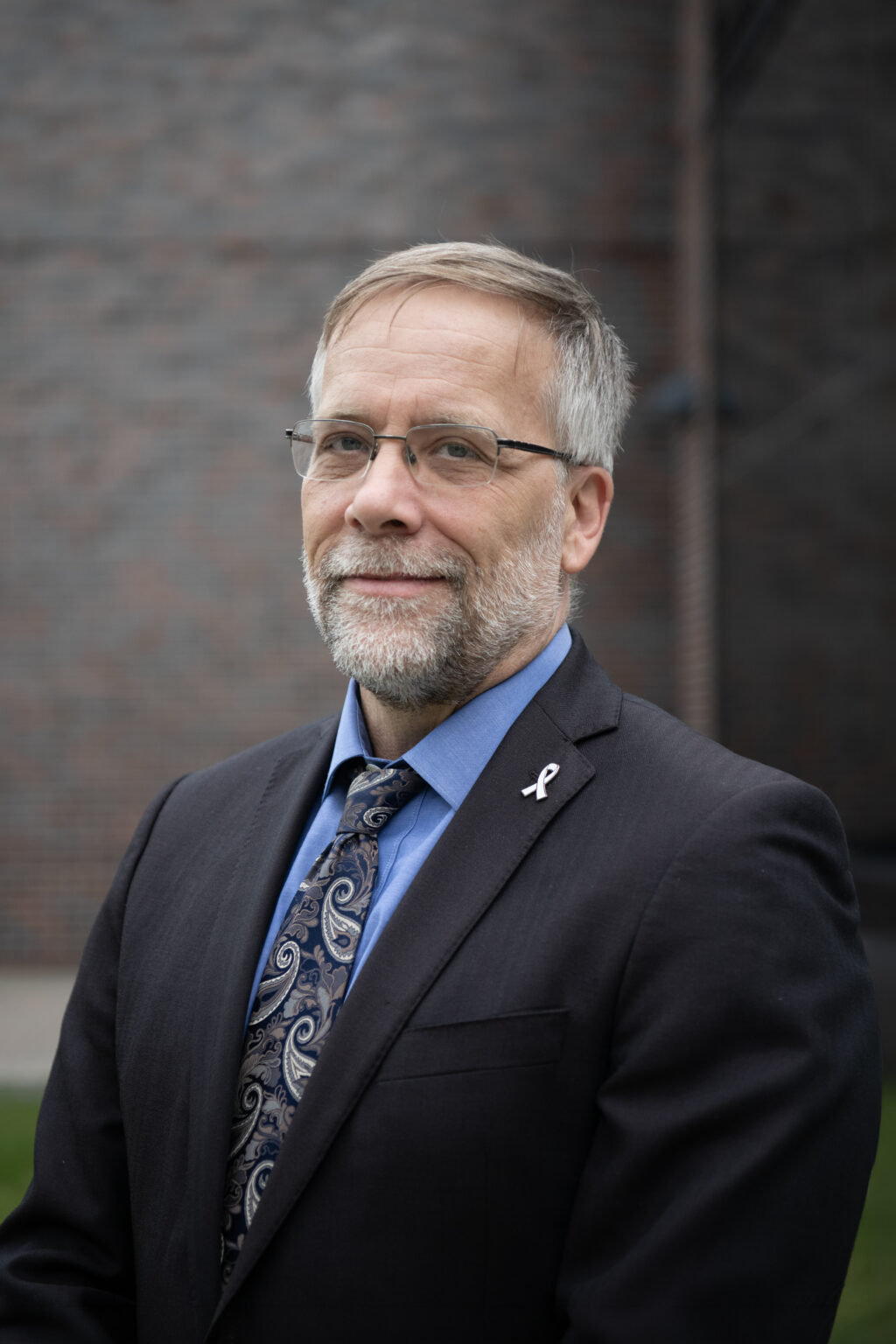 Ron Miller portrait outside in front of Minto Building at Carleton. He has a dark suit jacket and blue shirt.