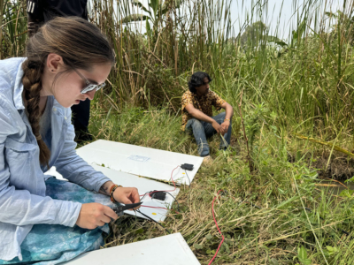 Students sitting in a field of tall grass in Uganda, setting up a solar project