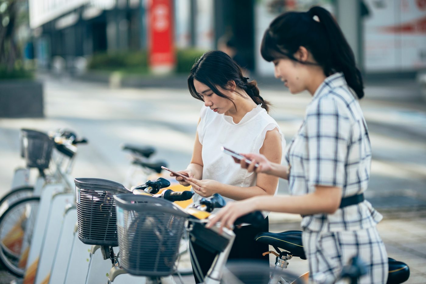 Two women using their smartphones to rent shared bicycles