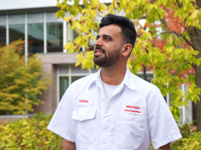 Male student in a Honda shirt standing in front of a building in autumn