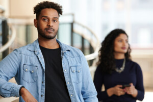 Two people standing. Black man/student in front and women/student slightly behind him.