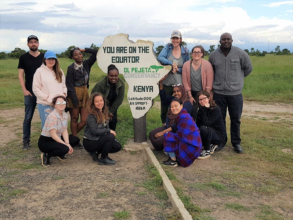 A group of people pose outdoors around a large Africa‑shaped equator sign at Ol Pejeta Conservancy in Kenya.