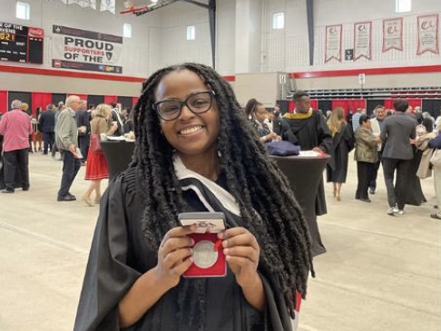 A graduating ESP student smiles at the camera and holds up the medal she has been awarded.