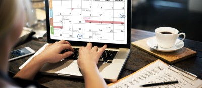 Woman typing on computer, looking at calendar on screen