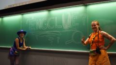 Two students at a chalkboard with EngClue written on board.