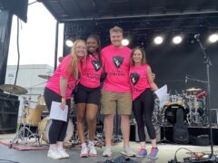Four students wearing pink ravens shirts on stage.