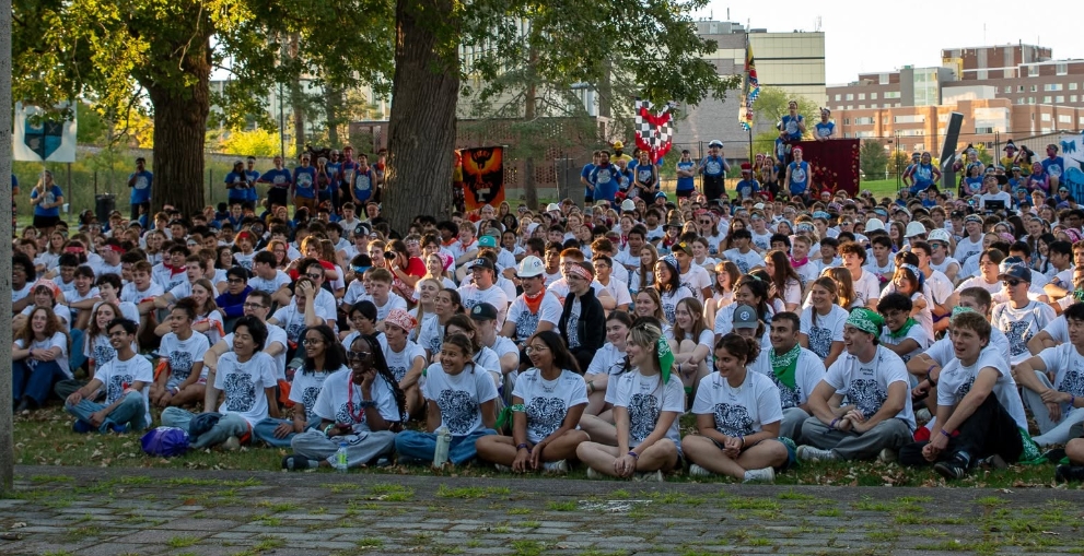 Students sitting with their teams outdoors at alumni field.