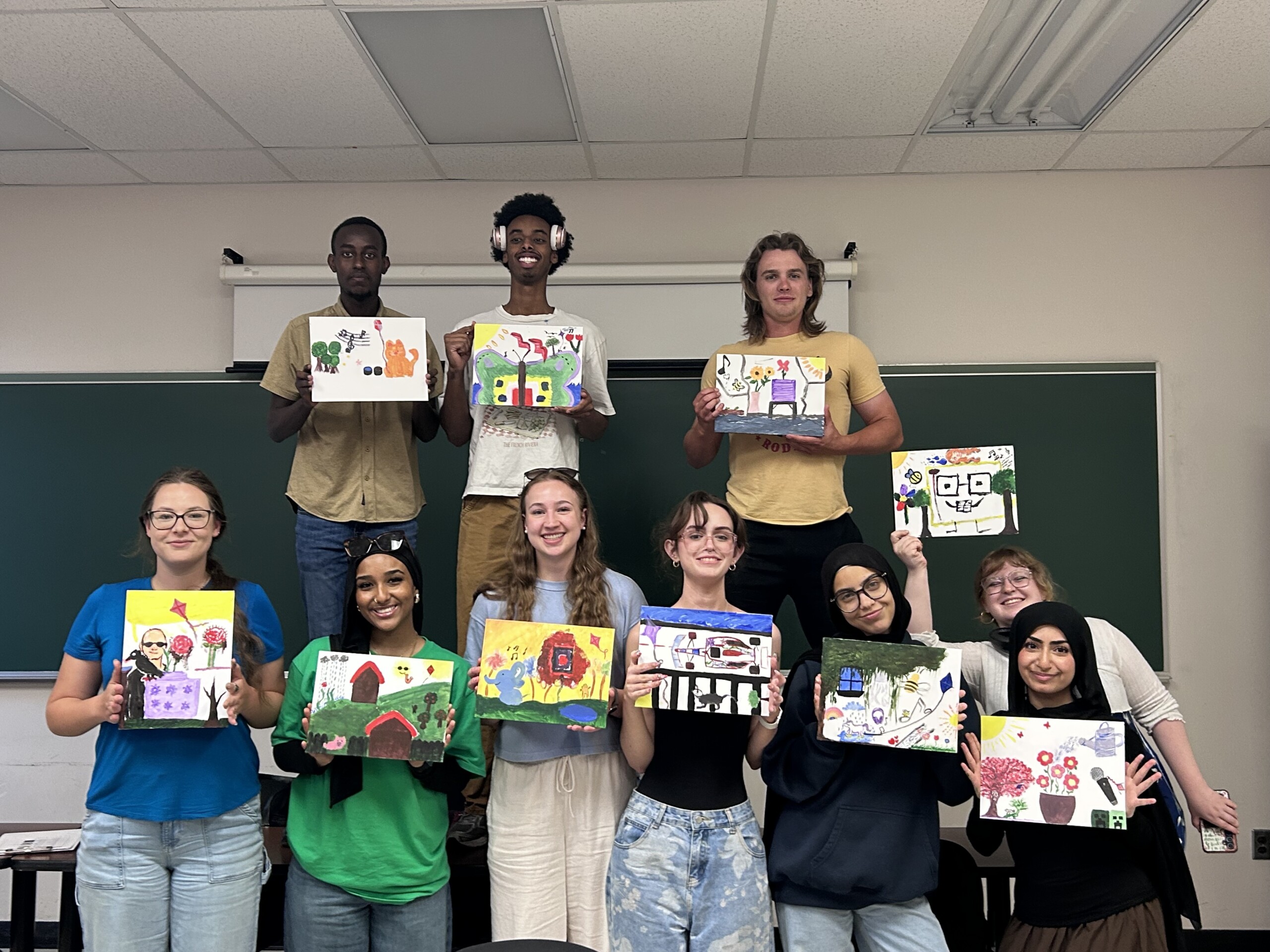 Students posing in a group while showing off their completed painted canvases.