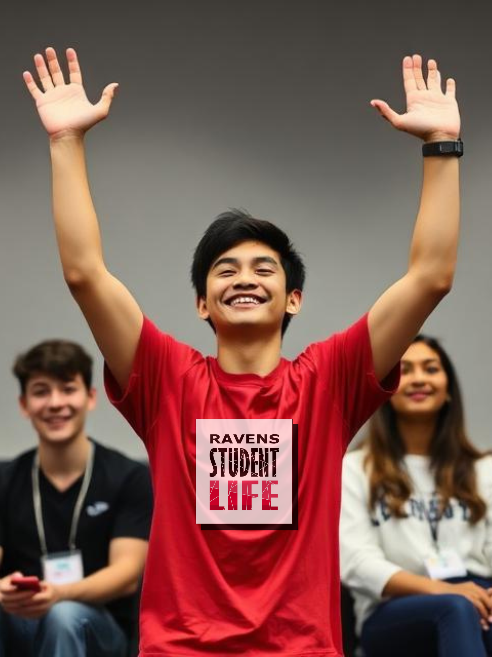 Student standing up with arms in the air as the won while two students sit on either side of them.