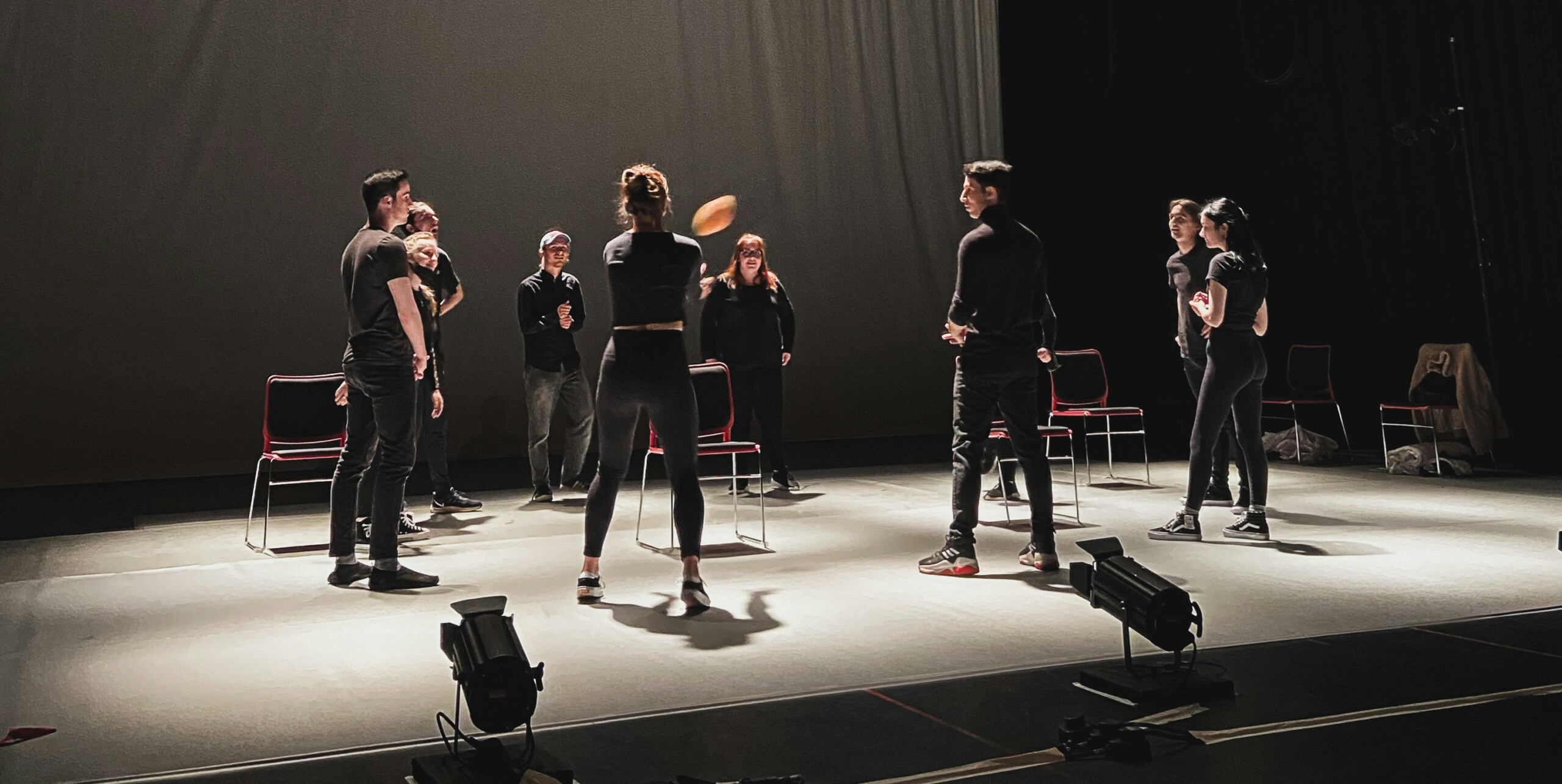 students on a stage while throwing a ball amongst themselves in a circle