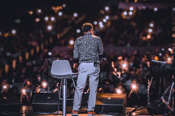 Comedian on stage with crowd in background.