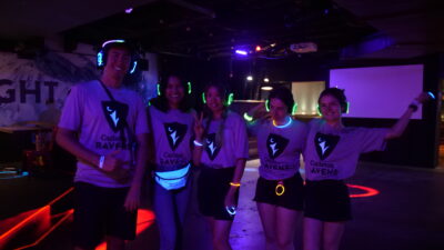 Students wearing ravens shirts that glow in the dark while holding neon glow headcu_people_phones at a dance.