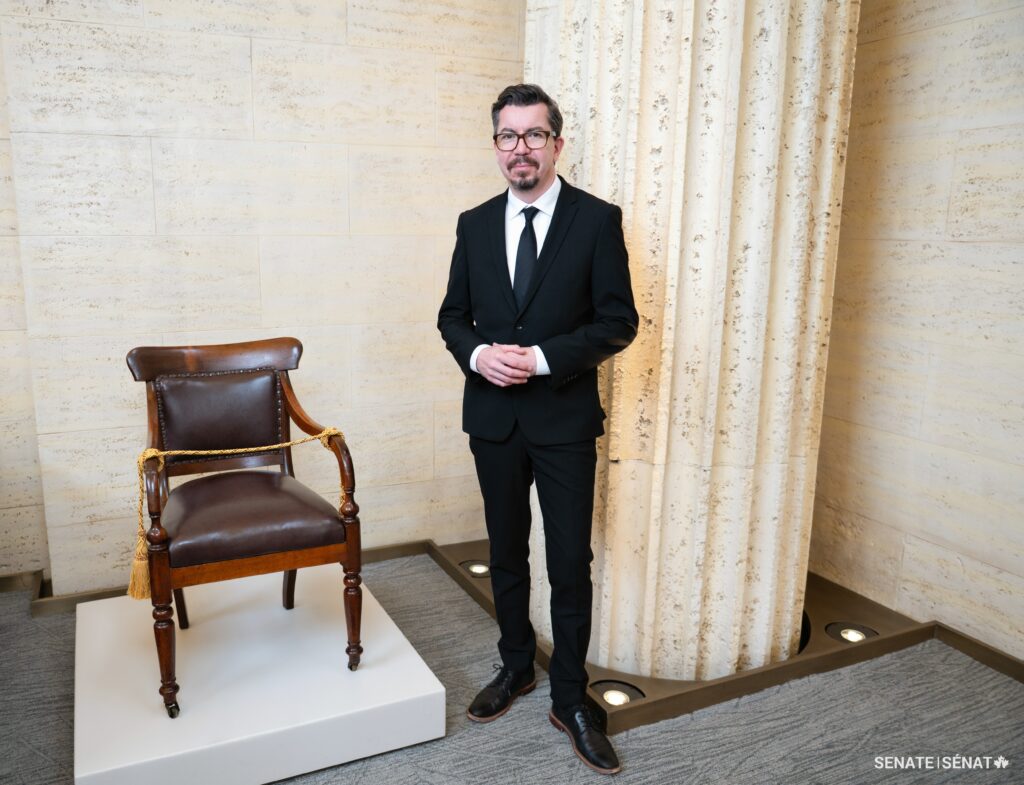 Mike Steinhauer standing next to an original Senate Chamber Chair saved from the fire of 1916.